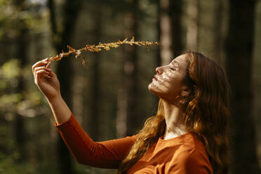 Close-up of beautiful woman with eyes closed holding plant in forest - TCEF00942