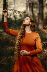 Beautiful woman with eyes closed holding leaves while standing in woodland - TCEF00944