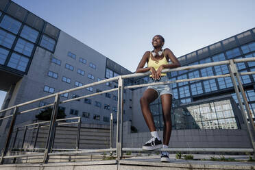 Smiling young woman looking away while standing by railing against building in city - MEUF01371