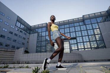 Young woman listening music and dancing against building in city - MEUF01373