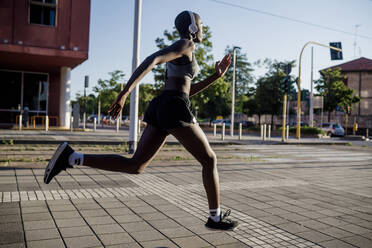 Weibliche Athletin hört Musik über Kopfhörer beim Laufen auf der Straße in der Stadt - MEUF01397