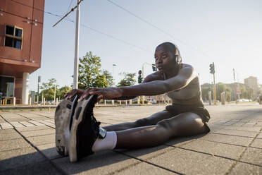 Female athlete listening music while exercising on street against clear sky in city - MEUF01404