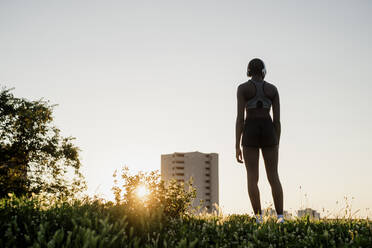 Junge Frau steht auf einer Wiese vor einem klaren Himmel bei Sonnenuntergang - MEUF01419