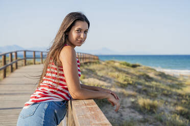 Schöne Teenager-Mädchen stehen auf Promenade am Strand gegen klaren blauen Himmel - DLTSF00859