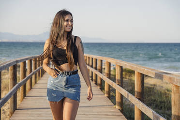 Schöne Teenager-Mädchen zu Fuß auf Promenade am Strand gegen klaren Himmel - DLTSF00869