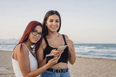 Teenager-Mädchen halten Smartphones am Strand gegen den klaren Himmel - DLTSF00875
