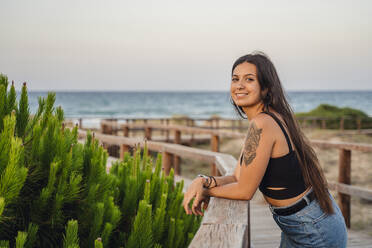 Glückliches Teenager-Mädchen auf der Promenade am Strand gegen den klaren Himmel stehend - DLTSF00879