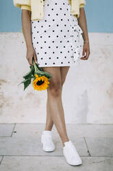Junge Frau in gepunktetem Kleid hält Sonnenblume, tiefer Ausschnitt - DCRF00420