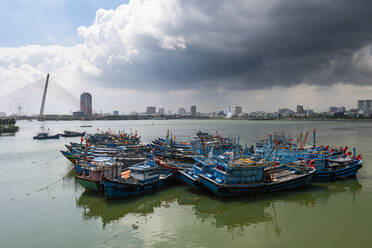 Vietnam, Da Nang, Storm clouds over old fishing boats moored in city harbor  stock photo