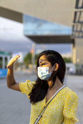 Young woman in mask shielding eyes while standing on city street - AFVF06786