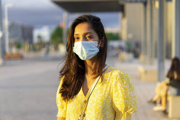 Junge Frau trägt eine Gesichtsmaske, während sie auf der Straße steht - AFVF06787