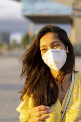 Happy young woman wearing face mask in city - AFVF06788