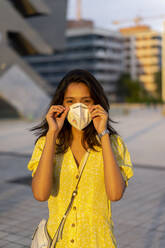 Young woman wearing face mask while standing in city - AFVF06791