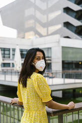 Junge Frau trägt Gesichtsmaske, während sie auf einem erhöhten Gehweg in der Stadt steht - AFVF06793