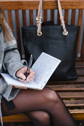 Frau, die auf einer Holzbank sitzend in ihr Tagebuch schreibt - JMPF00163