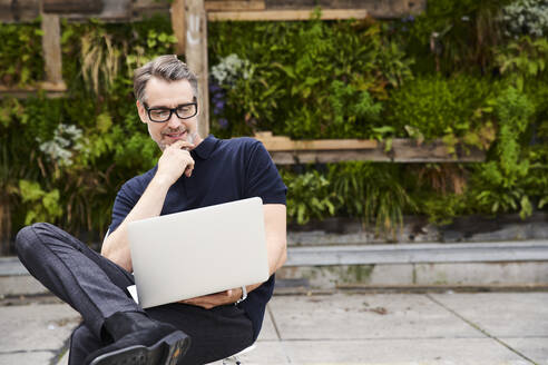Mature man using laptop while sitting on chair at yard - SUF00637