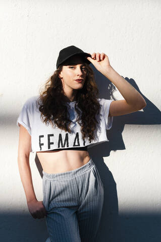 Fashionable young woman standing against white wall during sunny day stock photo