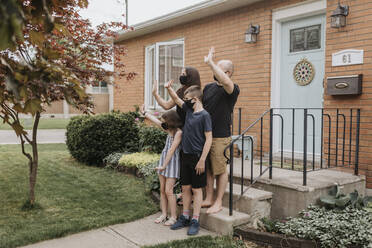 Family wearing masks waving hands while standing outside house in yard - SMSF00038