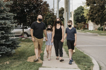 Family wearing masks holding hands while walking on footpath in city - SMSF00039