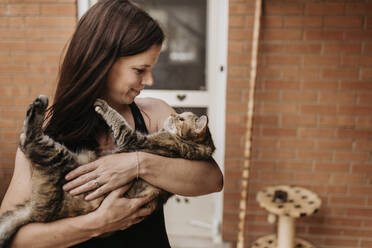 Close-up of mature woman carrying cat while standing against house - SMSF00050