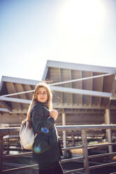 Businesswoman with backpack standing by railing against clear sky at station - EHF00522