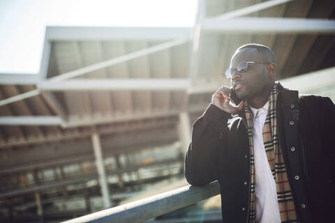 Stylish male professional talking over smart phone while standing by railing at station stock photo