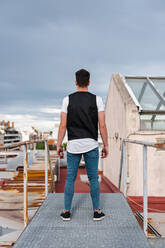 Junger Mann steht auf verlassener Terrasse gegen bewölkten Himmel - JMPF00187