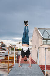 Young man doing handstand on abandoned terrace against cloudy sky - JMPF00188