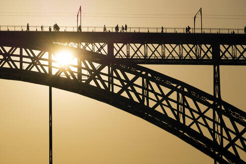 Silhouette der Brückenkonstruktion mit Menschen zu Fuß gegen helle goldene Sonnenlicht am Abend - ADSF01195