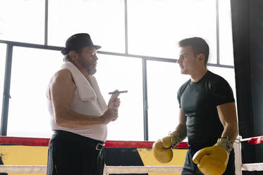 Seitenansicht eines erwachsenen Mannes mit Zigarre, der im Fitnessstudio einen Boxer trainiert. - ADSF01205