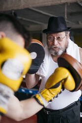 Side view of boxer man punching gloves of trainer in the gym. - ADSF01209