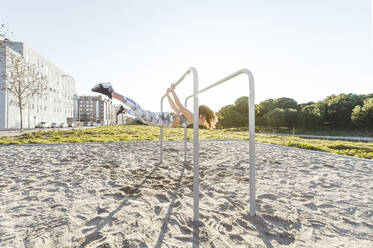 Side view of young lady doing exercise on parallel bars on court near building in sunny day - ADSF01229