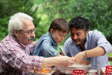 Drei Generationen einer männlichen Familie genießen eine gemeinsame Mahlzeit - CUF55779