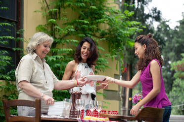 Three generations of female family preparing table for outdoor meal - CUF55788