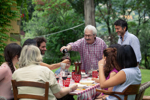 Älterer Mann schenkt beim Familienessen Wein ein - CUF55789