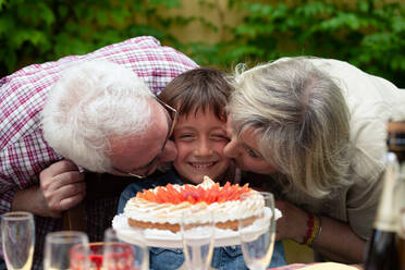 Junge mit Geburtstagskuchen, der von den Großeltern geküsst wird - CUF55793