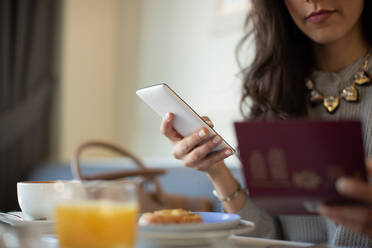 Ausgeschnittene Aufnahme einer jungen Frau mit digitalem Tablet, die elektronisch eincheckt, während sie in einem Boutique-Hotel in Italien frühstückt - CUF55798