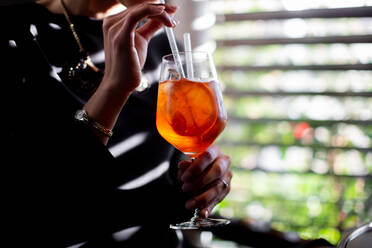 Cropped shot of young woman drinking spritz cocktail in boutique hotel restaurant, Italy - CUF55800