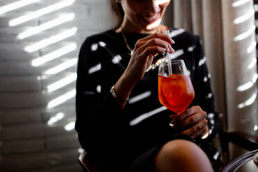 Abgeschnittene Aufnahme einer glücklichen jungen Frau, die im Restaurant eines Boutique-Hotels einen Schorle-Cocktail trinkt, Italien - CUF55803