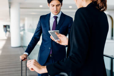 Businessman and businesswoman with wheeled luggage in hotel building - CUF55819