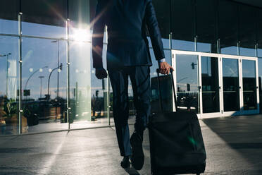 Businessman with wheeled luggage passing glass building, Malpensa, Milan - CUF55821