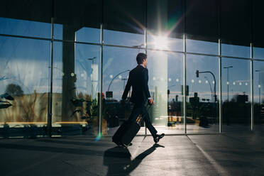 Businessman with wheeled luggage passing glass building, Malpensa, Milan - CUF55836