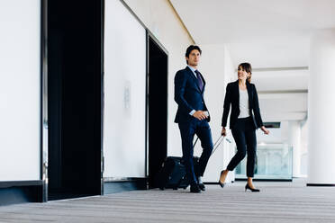 Businessman and businesswoman with wheeled luggage in hotel building - CUF55846