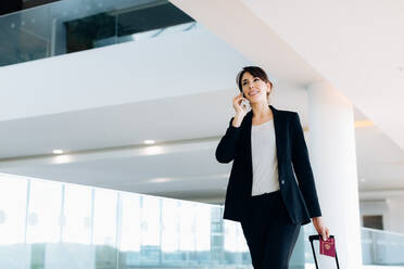 Businesswoman with wheeled luggage in hotel building - CUF55849