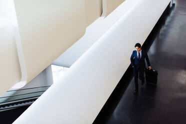 Businessman with wheeled luggage in hotel building - CUF55868