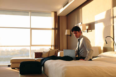 Geschäftsmann mit Laptop auf dem Bett eines Hotelzimmers - CUF55874