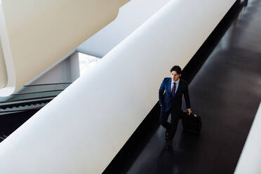 Businessman with wheeled luggage in hotel building - CUF55878