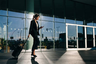 Businesswoman with wheeled luggage passing glass building, Malpensa, Milan - CUF55882