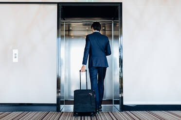 Geschäftsmann mit Gepäck auf Rädern beim Betreten eines Hotelaufzugs - CUF55891
