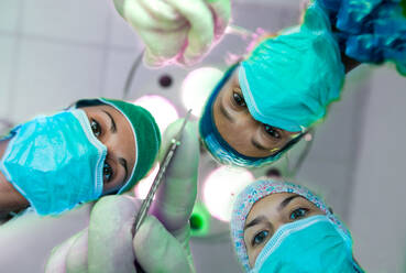Low angle view of three female surgeons wearing surgical masks looking at camera. - CUF55920